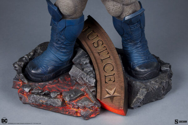 Darkseid DC Comics Maquette from Sideshow Collectibles. Close-up image of a superhero statue's feet clad in blue boots, standing on a base with rocks and a plaque inscribed with the word "JUSTICE".