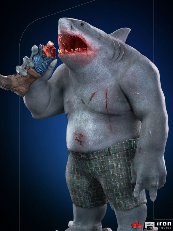 King Shark 1:10 Scale Statue from Iron Studios and DC Comics. A collectible figure of a shark-headed humanoid character wearing boxer shorts and a glove, holding a bitten-off leg.