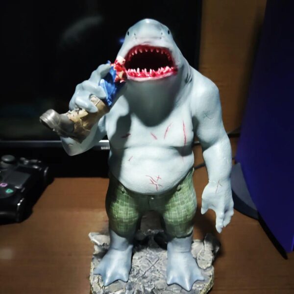 King Shark 1:10 Scale Statue from Iron Studios and DC Comics. A figurine of a shark-headed humanoid character wearing shorts, with scars on its body, holding a soda can near a gaming controller.