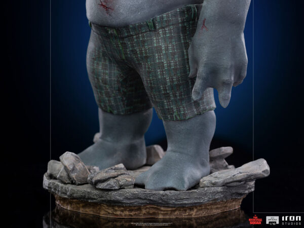 King Shark 1:10 Scale Statue from Iron Studios and DC Comics. Close-up image of a large figure's feet wearing plaid shorts, with rocky base details indicating a statue or figurine.