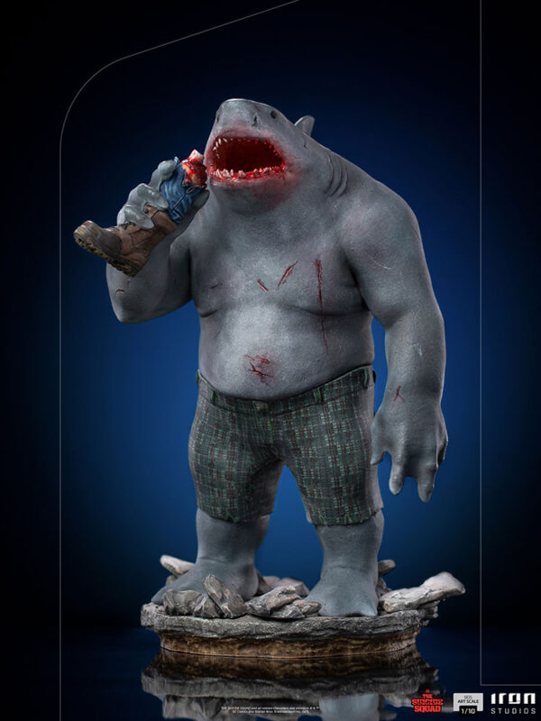 King Shark 1:10 Scale Statue from Iron Studios and DC Comics. A detailed collectible figure of a shark-headed humanoid character in shorts, holding a bitten ice cream cone, standing on a rock-like base against a dark blue background.