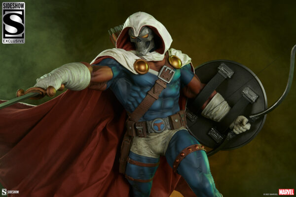 Marvel Taskmaster Premium Format Figure from Sideshow Collectibles. Close-up of a collectible figurine depicting a superhero archer, dressed in a blue and brown costume with a red cape and metallic mask, holding a bow and quiver with arrows against a green background.