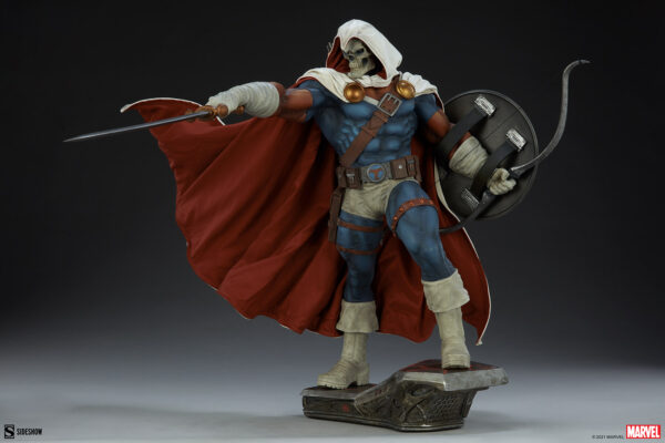 Marvel Taskmaster Premium Format Figure from Sideshow Collectibles. A high-quality statue of a character in a hooded white mask and skull face, red cape, wielding a sword and shield, standing on a themed pedestal.