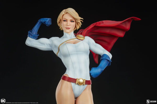 Power Girl Premium Format™ Figure from Sideshow Collectibles. A figurine of a blonde superheroine showing off her muscles, wearing a white suit with blue gloves and boots, a red cape, and a gold belt against a black background.