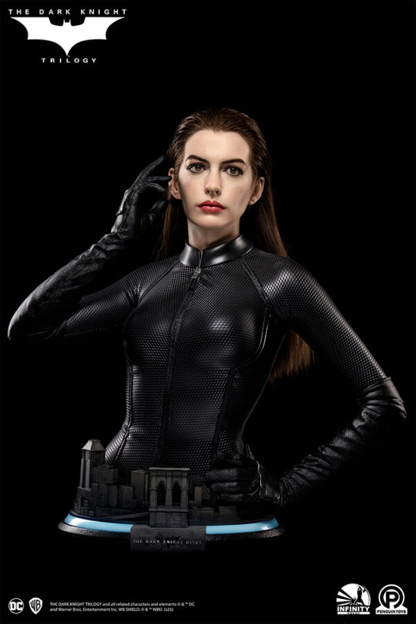 Catwoman (Selina Kyle) Life-Size Bust by Infinity Studio X Penguin Toys. Life-size bust of Catwoman (Selina Kyle), as portrayed by Anne Hathaway, wearing a sleek, textured black catsuit with her signature mask and cat ears. She stands in a poised stance with one hand adjusting her mask, capturing a determined expression. The base features miniature Gotham City buildings, including an archway labeled 'The Dark Knight Rises.'