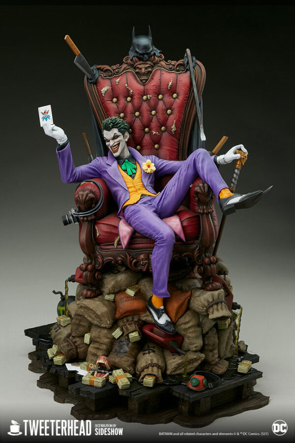 The Joker Deluxe Collector Edition Maquette from DC Comics and Tweeterhead. A collectible figure of The Joker seated on an ornate chair over a pile of money and trick items, with a Batman cowl hanging behind him.