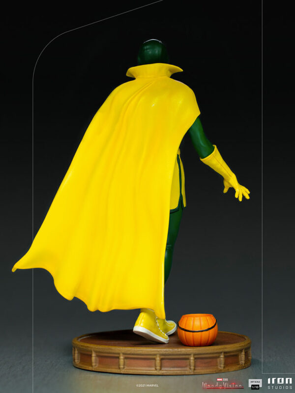 Vision Halloween Version WandaVision Art Scale 1:10 Statue from Marvel and Iron Studios. A collectible statue of a superhero character with green and yellow costume, and a flowing yellow cape, standing next to a small orange object on a wooden base.