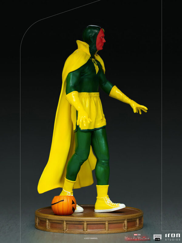 Vision Halloween Version WandaVision Art Scale 1:10 Statue from Marvel and Iron Studios. A collectible statue of a superhero in green and yellow costume with a cape, standing on a wooden base with a small pumpkin at its foot.