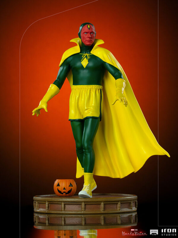 Vision Halloween Version WandaVision Art Scale 1:10 Statue from Marvel and Iron Studios. A collectible figurine of a superhero in a green and yellow costume with cape poised on a stand, with a small jack-o'-lantern at its feet and an orange background.